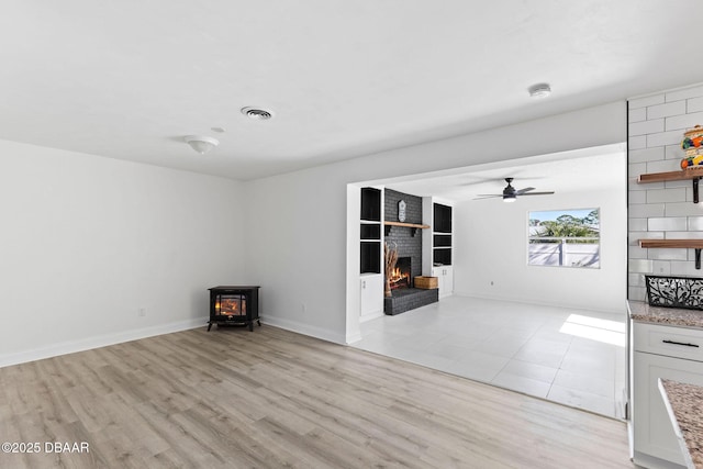 unfurnished living room featuring ceiling fan, a wood stove, a fireplace, and light hardwood / wood-style flooring