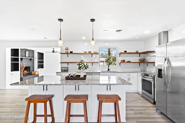 kitchen featuring stainless steel appliances, decorative light fixtures, a kitchen bar, decorative backsplash, and white cabinets