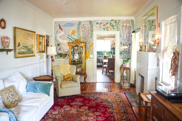 living area with wood finished floors, a fireplace, ornamental molding, and a wainscoted wall