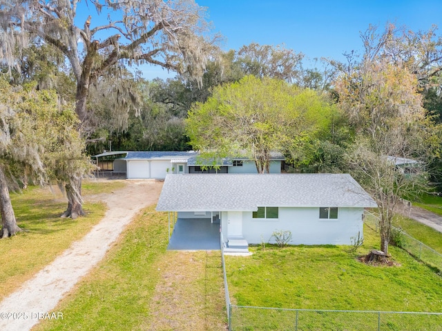 view of front of house featuring a shingled roof, a front lawn, fence, dirt driveway, and a carport