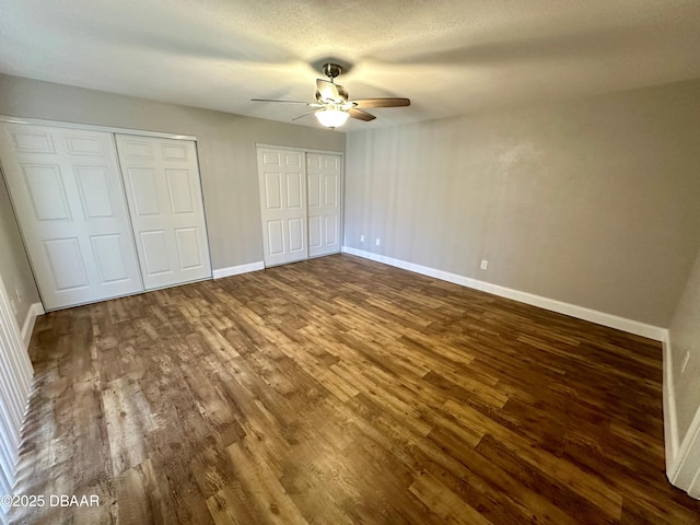 unfurnished bedroom with multiple closets, ceiling fan, dark hardwood / wood-style flooring, and a textured ceiling