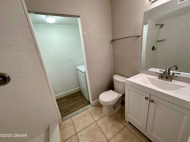 bathroom with tile patterned flooring, a tile shower, vanity, and toilet