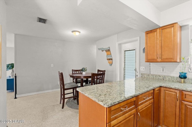 211 Fox Pl, Port Orange, FL 32127 - kitchen with decorative backsplash, light stone counters, a peninsula, and brown cabinetry