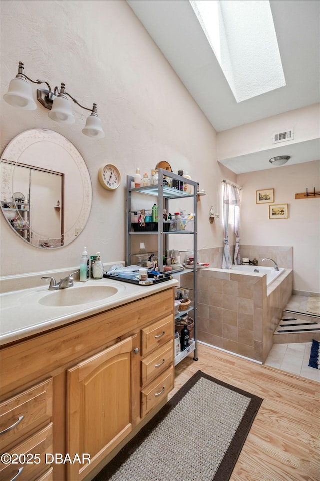 bathroom featuring a garden tub, vanity, visible vents, a skylight, and wood finished floors
