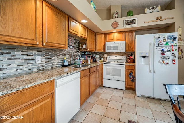kitchen with brown cabinetry, decorative backsplash, a sink, and white appliances