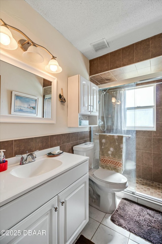 bathroom with a stall shower, a textured ceiling, visible vents, and tile walls