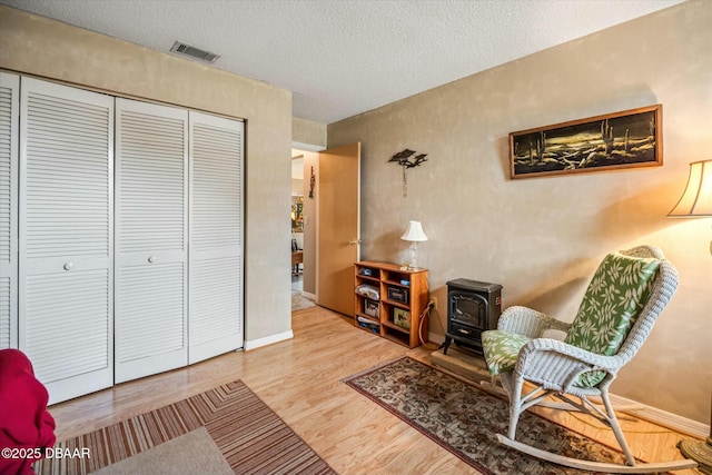 sitting room with baseboards, a textured ceiling, a wood stove, visible vents, and wood finished floors