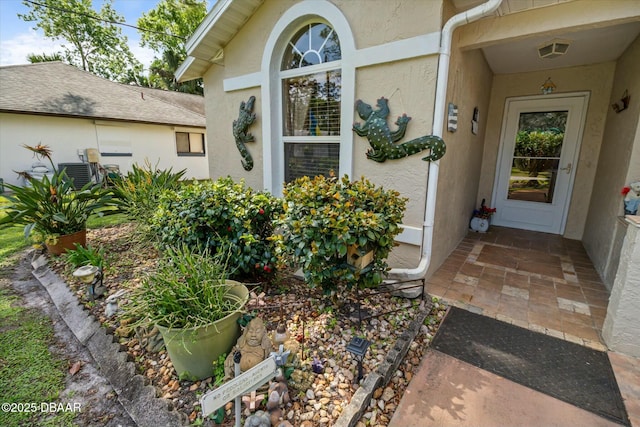 view of exterior entry with stucco siding, cooling unit, and visible vents