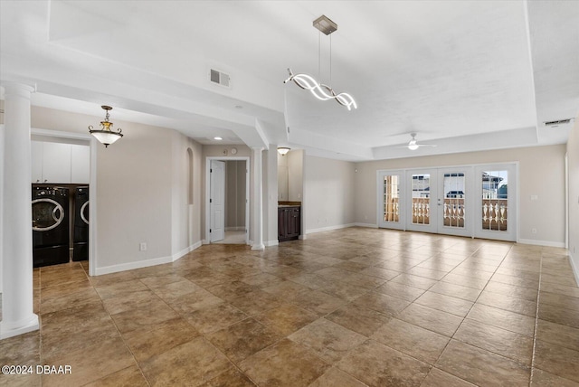 unfurnished living room with a raised ceiling, ornate columns, french doors, and independent washer and dryer