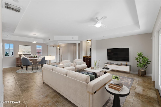 living room featuring ceiling fan with notable chandelier and a tray ceiling