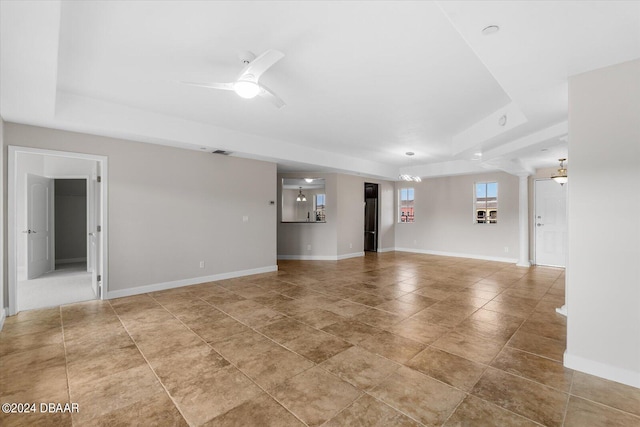 unfurnished living room with ceiling fan, a raised ceiling, and ornate columns