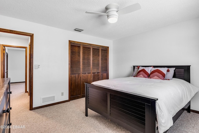 bedroom with ceiling fan, light colored carpet, a closet, and a textured ceiling