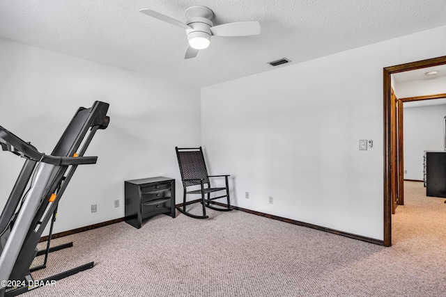 exercise room with ceiling fan, light colored carpet, and a textured ceiling