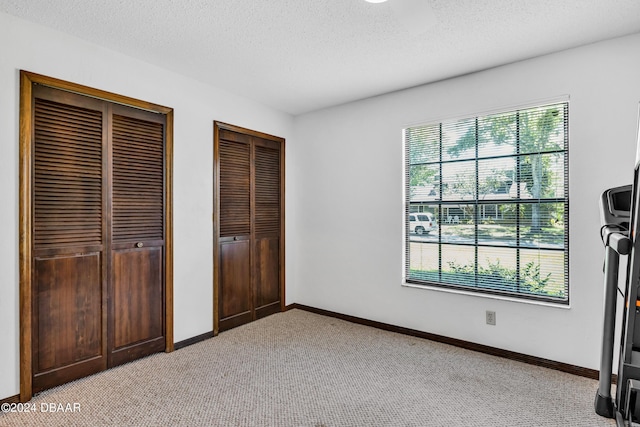 unfurnished bedroom with a textured ceiling, light carpet, and two closets