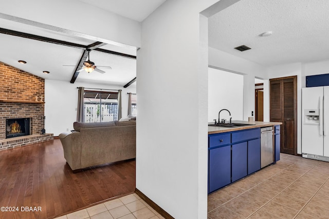 kitchen with sink, dishwasher, a fireplace, white fridge with ice dispenser, and a textured ceiling