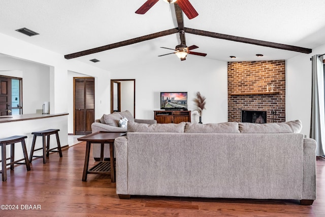 living room featuring a brick fireplace, dark hardwood / wood-style floors, vaulted ceiling with beams, and a textured ceiling