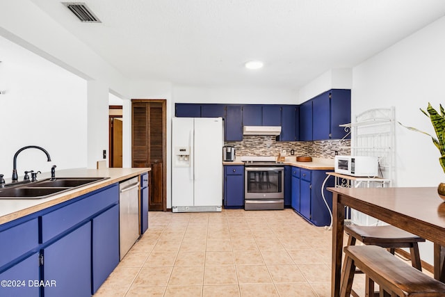 kitchen with appliances with stainless steel finishes, tasteful backsplash, sink, light tile patterned floors, and blue cabinetry