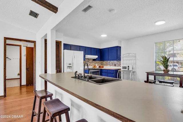 kitchen with white appliances, light hardwood / wood-style flooring, backsplash, a kitchen breakfast bar, and blue cabinets