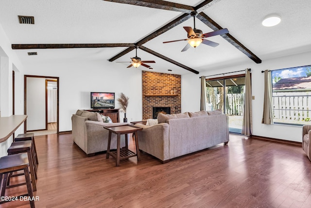 living room featuring a brick fireplace, dark hardwood / wood-style floors, vaulted ceiling with beams, and a textured ceiling