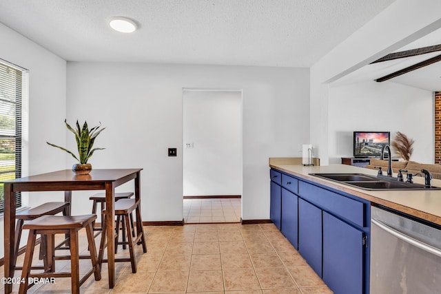 kitchen with light tile patterned flooring, blue cabinets, sink, stainless steel dishwasher, and a textured ceiling