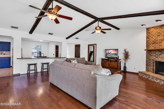 living room with ceiling fan, dark hardwood / wood-style flooring, a brick fireplace, and vaulted ceiling with beams