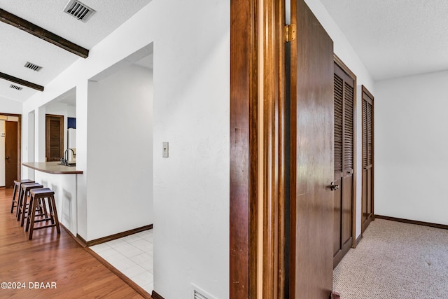 corridor with beam ceiling, sink, a textured ceiling, and light hardwood / wood-style flooring