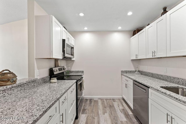 kitchen with stainless steel appliances, white cabinetry, light stone counters, and light hardwood / wood-style floors