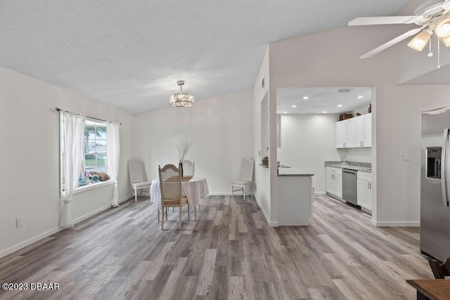 unfurnished dining area with ceiling fan with notable chandelier, a textured ceiling, and light hardwood / wood-style floors