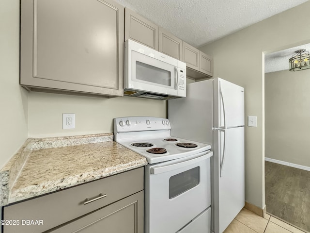 kitchen featuring baseboards, gray cabinets, light tile patterned flooring, white appliances, and a textured ceiling