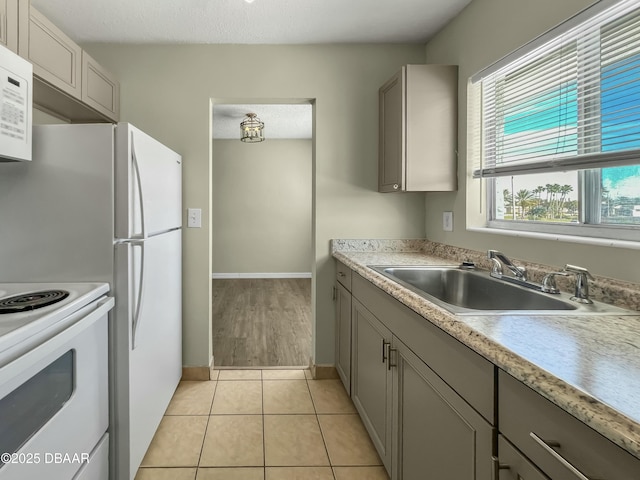 kitchen featuring gray cabinets, a sink, white appliances, light countertops, and light tile patterned floors