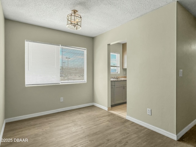 empty room with a sink, baseboards, a textured ceiling, and light wood-style flooring