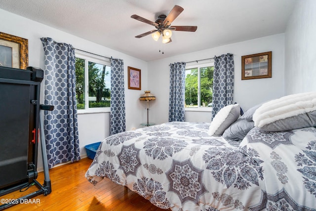 bedroom featuring hardwood / wood-style flooring, a ceiling fan, and multiple windows