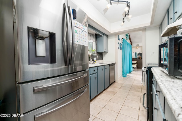 kitchen with light tile patterned floors, a sink, appliances with stainless steel finishes, a tray ceiling, and backsplash