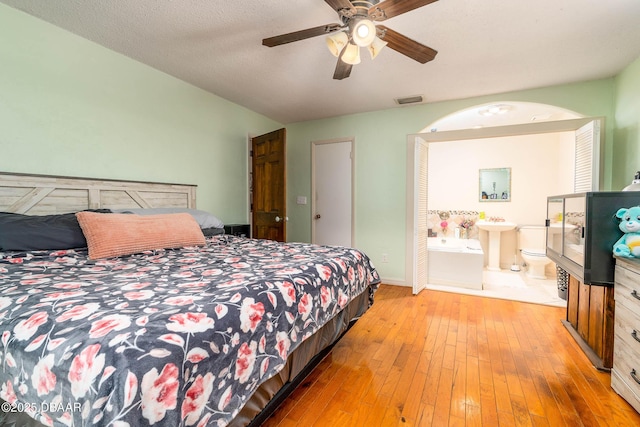 bedroom featuring a sink, visible vents, ceiling fan, wood-type flooring, and ensuite bath
