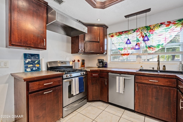 kitchen with wall chimney range hood, appliances with stainless steel finishes, light tile patterned floors, hanging light fixtures, and sink