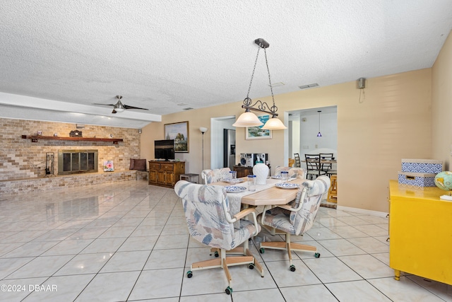 dining space with light tile patterned flooring, a textured ceiling, ceiling fan, and a brick fireplace