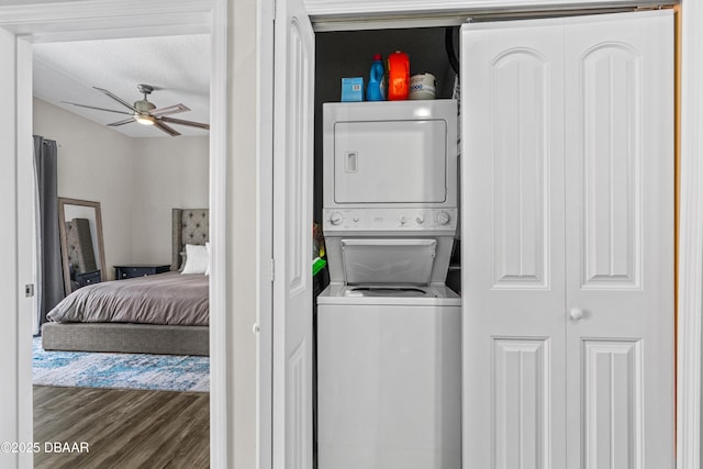 laundry area featuring wood finished floors, stacked washer and clothes dryer, a ceiling fan, and laundry area