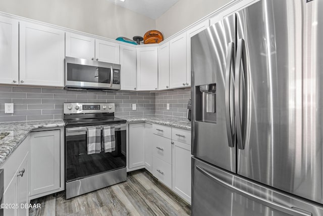 kitchen featuring light stone countertops, tasteful backsplash, light wood-style flooring, white cabinets, and appliances with stainless steel finishes