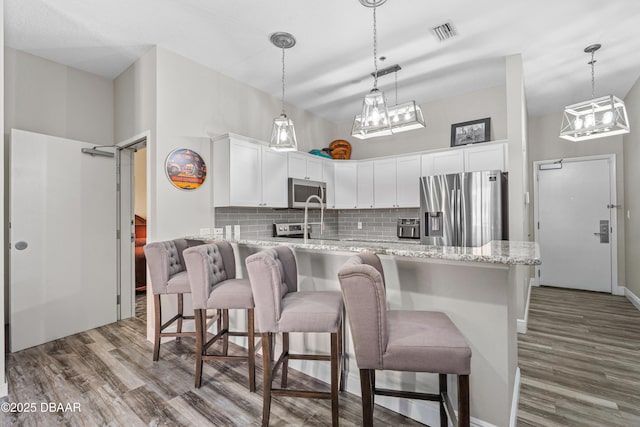kitchen with tasteful backsplash, wood finished floors, appliances with stainless steel finishes, white cabinets, and visible vents