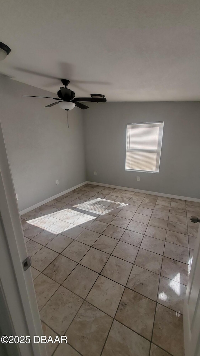 empty room with light tile patterned floors, a ceiling fan, and baseboards