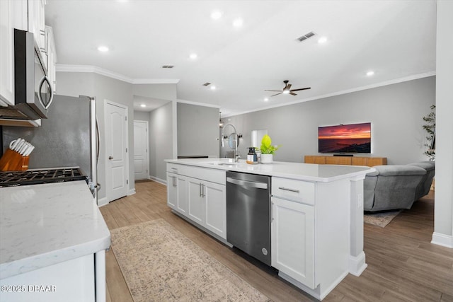 kitchen with ceiling fan, crown molding, an island with sink, white cabinets, and appliances with stainless steel finishes