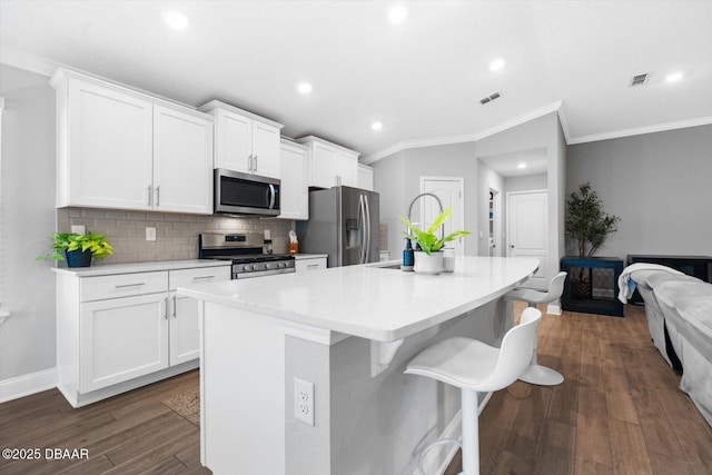 kitchen with white cabinets, appliances with stainless steel finishes, dark hardwood / wood-style flooring, and an island with sink