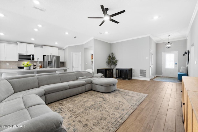 living room featuring ceiling fan with notable chandelier, light hardwood / wood-style floors, ornamental molding, and sink