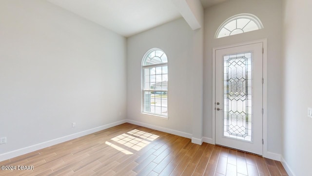 entryway featuring light wood finished floors, beam ceiling, and baseboards