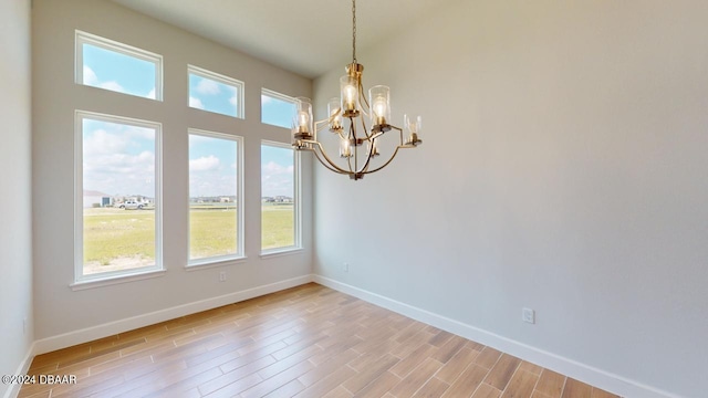 spare room featuring a notable chandelier, a healthy amount of sunlight, baseboards, and light wood finished floors