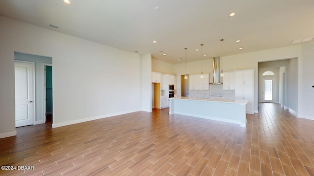 kitchen with white cabinetry, open floor plan, wall chimney range hood, and visible vents