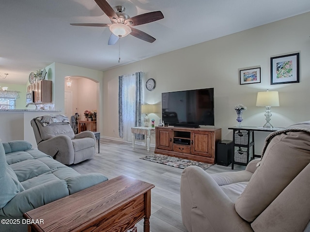 living room featuring light wood finished floors, a ceiling fan, baseboards, and arched walkways