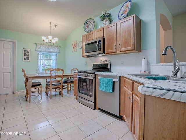 kitchen with lofted ceiling, light tile patterned floors, a sink, a chandelier, and appliances with stainless steel finishes