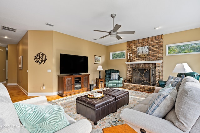 living room with a brick fireplace, wood-type flooring, a healthy amount of sunlight, and ceiling fan