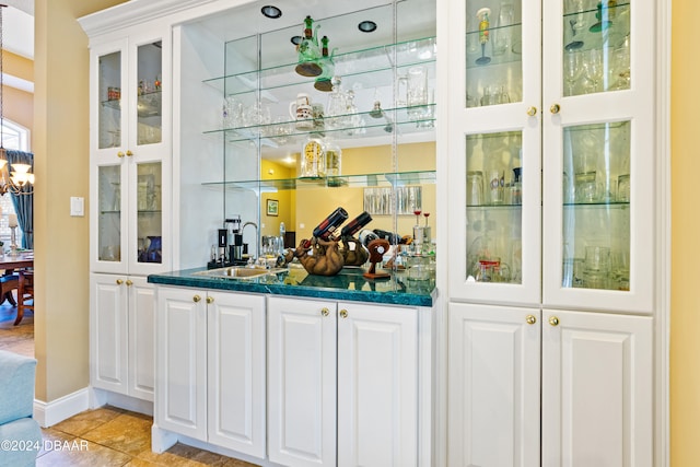 bar with white cabinets, dark stone counters, sink, and light tile patterned flooring